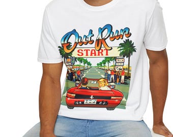 May include: A white short-sleeve t-shirt featuring a colorful graphic print of a red sports car on a road with palm trees. The text Out Run is written in a blue and orange gradient font above the word START in red capital letters.