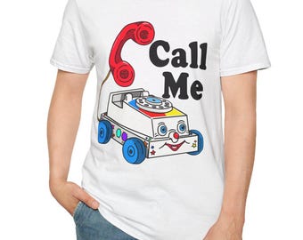 May include: White t-shirt featuring a cartoon illustration of a toy phone with the text "Call Me". The phone is red, and the toy car is white with blue wheels and colorful accents. A fun and playful design.