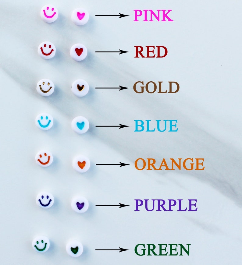 Op de afbeelding: Een set witte kralen met smiley-gezichten en harten in verschillende kleuren. De kleuren zijn roze, rood, goud, blauw, orange, paars en groen.