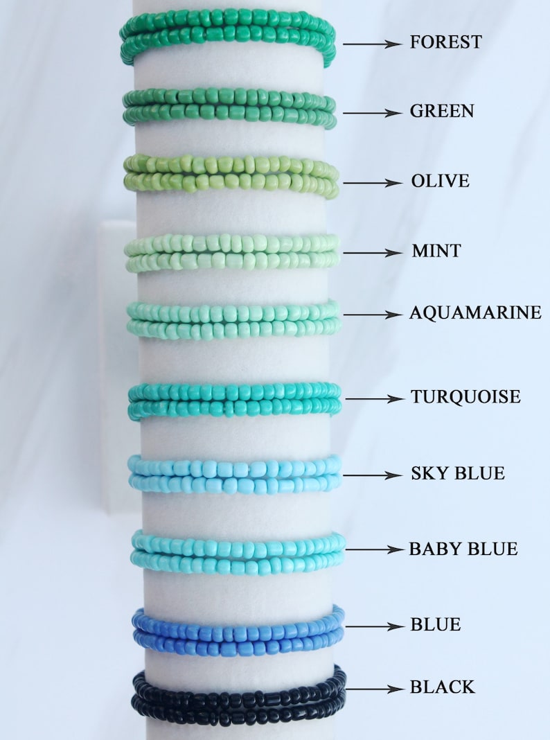 Op de afbeelding: Een set van tien kralenarmbanden in verschillende tinten groen, blauw en zwart. De armbanden zijn verticaal gerangschikt, met de donkerste kleur onderaan en de lichtste kleur bovenaan. De kleuren zijn van boven naar beneden gelabeld: Forest, Green, Olive, Mint, Aquamarine, Turquoise, Sky Blue, Baby Blue, Blue en Black.