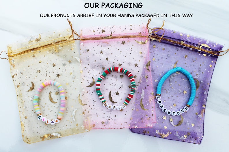 Op de afbeelding: Drie kleurrijke kralenarmbanden met gepersonaliseerde namen, Ella, Maria en Erastour, verpakt in individuele mesh-zakjes met een sterpatroon.