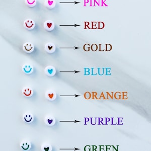 Pode incluir: Um conjunto de contas brancas com carinhas sorridentes e cora&ccedil;&otilde;es em diferentes cores. As cores s&atilde;o rosa, vermelho, dourado, azul, laranja, roxo e verde.