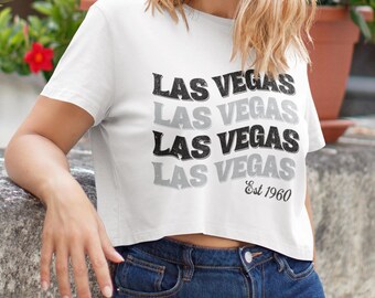 May include: White cropped t-shirt with a black and grey graphic print that says "Las Vegas" four times and "Est 1960" underneath.