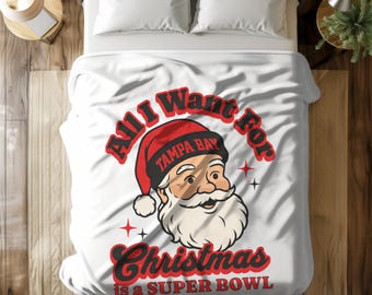 May include: White bedspread featuring a Santa Claus graphic wearing a red hat with "TAMPA BAY" text. The text "All I Want For Christmas is a Super Bowl" is in red. The bedding is on a bed with white pillows.