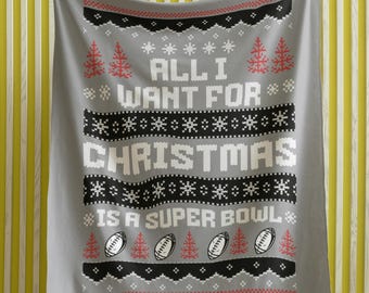 May include: Gray fleece blanket with a Christmas-themed design. The blanket features a white knit pattern with the text "All I Want For Christmas Is A Super Bowl" and red and black footballs.