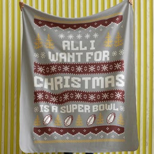 May include: Gray fleece blanket with a red and white knitted pattern. The blanket features the text "All I Want For Christmas Is A Super Bowl" with a football graphic.
