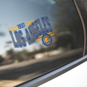 May include: A blue and yellow Los Angeles Rams decal with the text "1937 LOS ANGELES" and a logo of a football helmet with the text "FOOTBALL" and "1937" inside a circle.