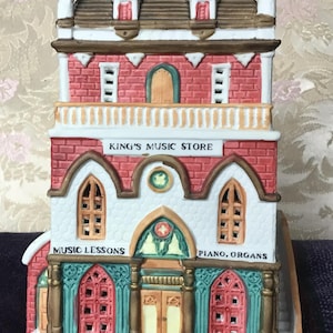 May include: A red brick building with a white facade and a green roof. The building has a sign that reads "King's Music Store". There are windows on the front of the building, and a door with a sign that reads "Music Lessons".