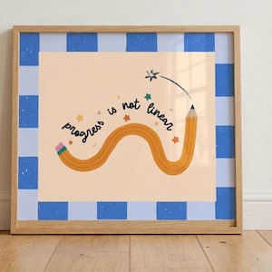 May include: A square framed print featuring a light peach background with a wavy orange pencil illustration and the text "progress is not linear" in black script. The border consists of a blue and light blue checkered pattern with a wooden frame.