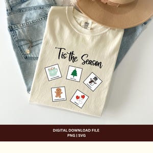 May include: A beige t-shirt with the text "'Tis the Season" printed in black. There are five small squares with illustrations of a cup of hot chocolate, a Christmas tree, a snowman, a gingerbread man, and mittens.