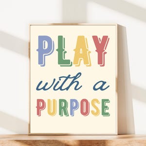 May include: A framed print with the words "PLAY with a PURPOSE" in colorful, bold letters. The word "PLAY" is in blue, green, yellow, and red. The words "with a" are in a dark blue script, and "PURPOSE" is in red, yellow, green, and blue.