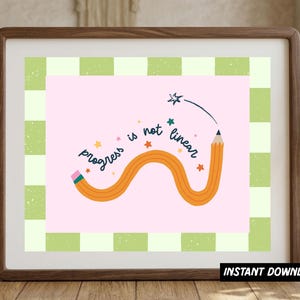 May include: A framed wall art print featuring a light pink background with a wavy orange pencil illustration. The text "progress is not linear" is written in dark blue script, surrounded by small orange and teal stars. A green and white checkered border frames the central design.