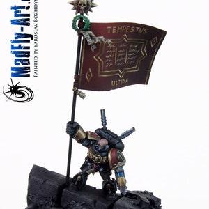 以下が含まれることがあります： 「Tempestus Ultima」と書かれた旗を持った黒と赤のスペースマリーンのミニチュア。旗は赤地に金色の文字で、上部に頭蓋骨が飾られている。ミニチュアは黒い岩の台座の上に立っている。