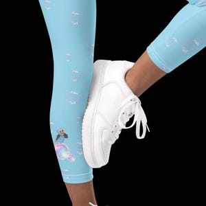 May include: Blue leggings with a white and light blue bubble pattern. A cartoon character is sitting on a bubble. The leggings are being worn by a person wearing white sneakers.