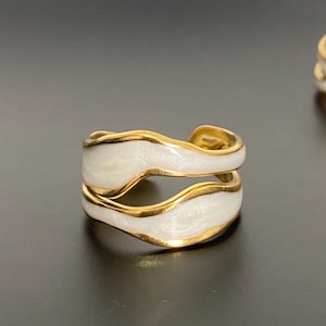 May include: Two gold rings with white enamel. The rings are designed with a wavy, organic shape.