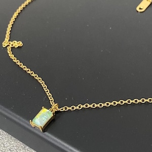 May include: A gold chain necklace with a small rectangular pendant featuring a green and blue gemstone.