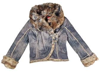 Puede incluir: Chaqueta azul con cuello y puños de piel sintética. La chaqueta tiene un aspecto desgastado con ribetes color crema y cierres de palanca. La piel sintética es marrón y beige.