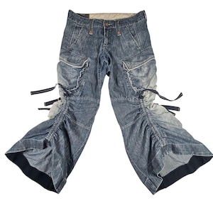 May include: Blue denim cargo trousers with multiple pockets and unique ruffled and cinched leg details. The trousers have a low waist and feature dark blue accents. The design includes adjustable straps and a distinctive, stylish appearance.