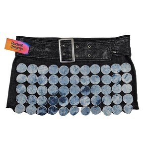 Può includere: Gonna di jeans nera con cintura in pelle e fibbia argentata. La gonna è impreziosita da cerchi di jeans blu chiaro. Un'etichetta con la scritta "Radical Dreams" è attaccata.