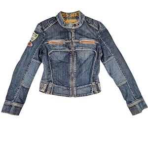 May include: A blue denim jacket with a zip-up front, featuring orange accents and patches. The jacket has a stand-up collar and a fitted silhouette. The sleeves are long, and the jacket has a distressed look.