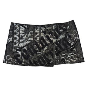 May include: A black and silver mini skirt with a textured, abstract pattern. The skirt has a wrap-style design and a metallic sheen. The pattern includes circles and vertical lines.