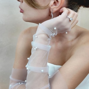 May include: White sheer gloves with pearl embellishments. The gloves are long and reach to the elbow. The pearls are evenly spaced and create a delicate and elegant look.