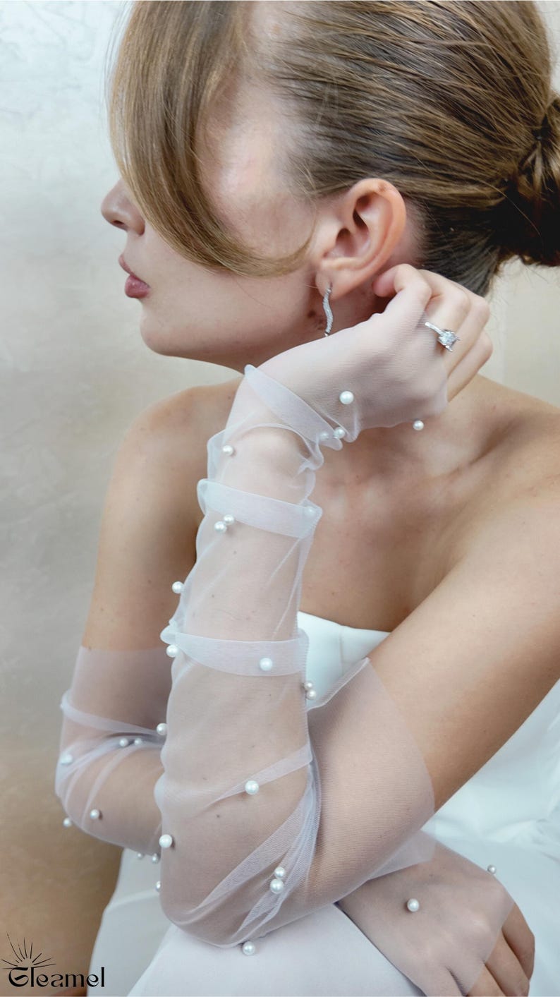 May include: White sheer gloves with pearl embellishments. The gloves are long and reach to the elbow. The pearls are evenly spaced and create a delicate and elegant look.