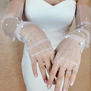May include: White tulle bridal gloves with pearl embellishments. The gloves have the text "To Have & To Hold" and "To Love & To Cherish" written on them.