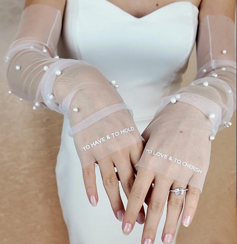 May include: White tulle bridal gloves with pearl embellishments. The gloves have the text "To Have & To Hold" and "To Love & To Cherish" written on them.