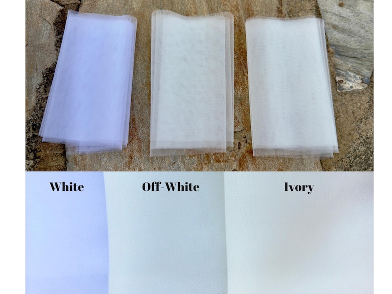 May include: Three swatches of tulle fabric in white, off-white, and ivory. The swatches are laid out on a textured surface.