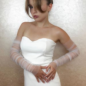 May include: A white strapless dress with sheer tulle sleeves. The sleeves are gathered at the wrist and have a delicate, flowing look.