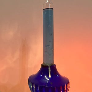 May include: A blue glass Christmas light bulb with a blue glass base. The bulb is filled with a blue liquid.