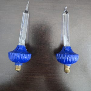 May include: Two vintage Christmas lights with blue plastic bases and clear glass bulbs.