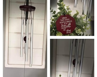 May include: A silver wind chime with a red wooden top and two red hexagonal tags. The tags have white text that reads "Know that every gentle breeze is a Love Note from Me Dad 1947-2009" and "The Szumanski Home Sweet Home".