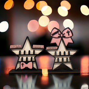 May include: Two white star-shaped wooden shelves with black trim and a pink bow with a cross on top. The shelves are labeled "BRANTLEE ALLSTAR" and "ALLSTAR".