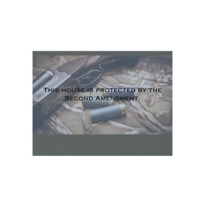 May include: A shotgun and two shotgun shells on a camouflage patterned surface. The text "This house is protected by the Second Amendment." is printed on the image.