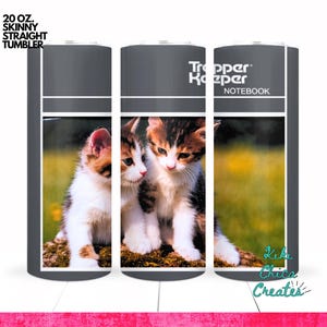 May include: A 20 oz. skinny straight tumbler featuring a photograph of two kittens. The tumbler has a gray top and bottom with the words "Trapper Keeper Notebook" printed on the side. The kittens are brown, white, and black.