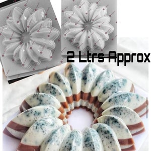 Peut inclure: Un moule en plastique blanc en forme de fleur à 12 pétales. Le moule est conçu pour faire un dessert de 2 litres. Le texte "IDEA DE LA" et un symbole de globe terrestre sont visibles en arrière-plan.