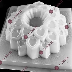 Op de afbeelding: Een witte plastic mal in de vorm van een ring van harten. De mal is ontworpen om een ​​taart of gelei-dessert te maken met een ringvorm en een hartpatroon.