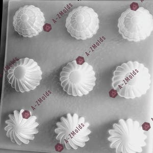 May include: A silicone mold with eight cavities for making decorative cake toppers. The mold features two different designs, each with a flower-like pattern. The mold is white and has a smooth surface.