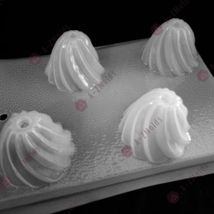 May include: A clear plastic mold with four cavities shaped like small, round cakes with a swirl design. The mold is designed for making small cakes or other desserts.