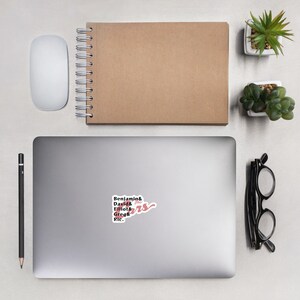 May include: A white laptop computer with a sticker that says "Benjamin & David & Elliot & Greg & Ric." The sticker is pink and white and has a handwritten-style font.