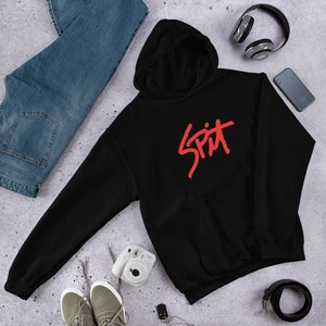 May include: Black hooded sweatshirt with a red "SPIT" logo printed on the front. The sweatshirt is laid flat on a gray surface with a pair of jeans, a camera, headphones, and a key chain.