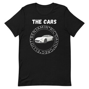 May include: Black t-shirt with a white circle graphic featuring a white sports car and the text "THE CARS *GREG* *ELLIOT* *BENJAMIN* *RIC* *DAVID*"