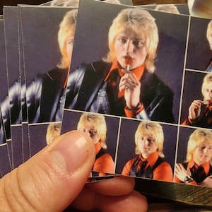 May include: A collage of images featuring a person with blonde hair wearing a black leather jacket and a red shirt. The person is holding a lollipop in some of the images.