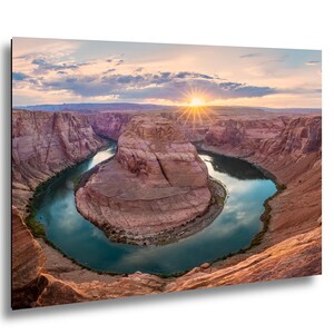 Könnte beinhalten: Ein Landschaftsdruck von Horseshoe Bend bei Sonnenuntergang. Das Bild zeigt die hufeisenförmige Biegung des Colorado River, umgeben von roten Felswänden. Die Sonnenstrahlen brechen durch die Wolken und beleuchten das Wasser und die Landschaft.