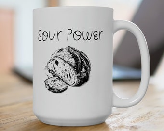 May include: White ceramic mug with a black and white illustration of a loaf of bread and the text "Sour Power".