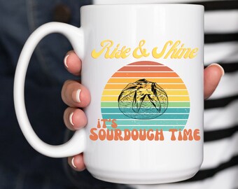 May include: White ceramic mug with a retro-style sunrise graphic and the text "Rise & Shine it's sourdough time".
