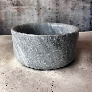 May include: A grey marble bowl with a smooth, polished surface. The bowl is round and has a slightly flared rim.