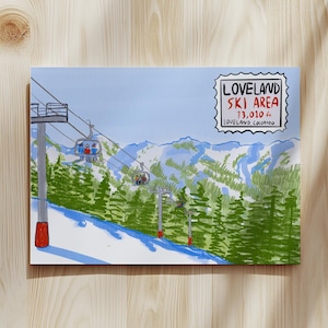 Pode incluir: Uma impressão ilustrada em tela da área de esqui de Loveland, no Colorado. A obra de arte retrata um teleférico com esquiadores, montanhas cobertas de neve e árvores perenes. A impressão inclui o texto "LOVELAND SKI AREA 13,010 ft LOVELAND, COLORADO."